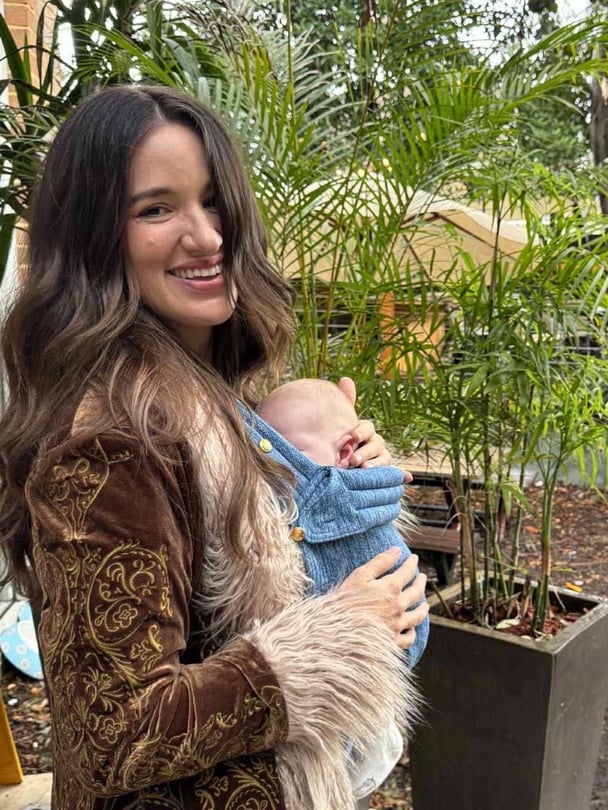 Mel smiles with baby Joey in baby carrier.