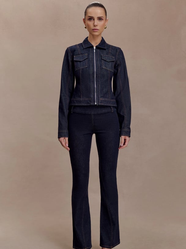 Woman with dark hair pulled back in a sleek wearing an indigo-wash denim jacket and flared denim jeans.