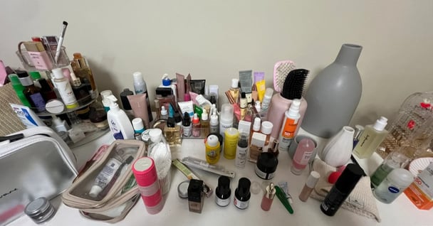 A very messy, disorganised dresser. Beauty products are scattered on the dresser top.