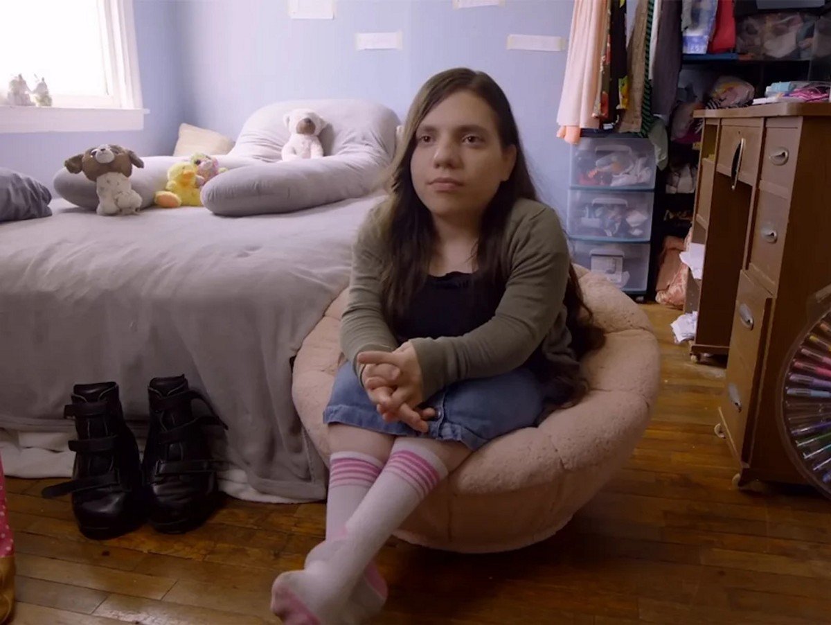 Natalia Grace sitting in a chair from a scene in The Curious Cause of Natalia Grace. 