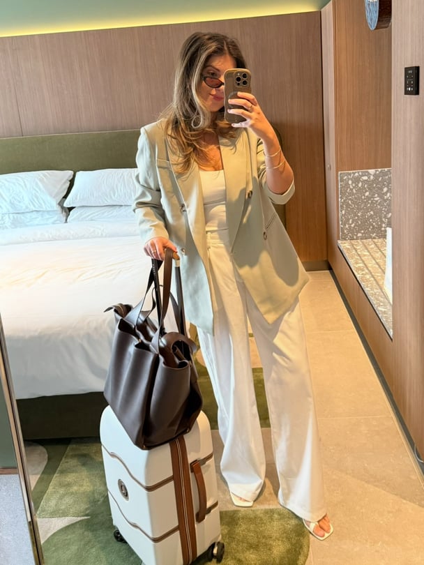 Mirror selfie of Paige holding her suitcase in hotel room.