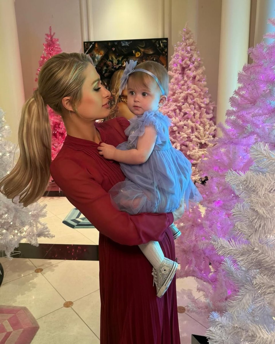 Paris Hilton holds her baby daughter London, posing in front of their Christmas trees, which are a range of different shades of pink.