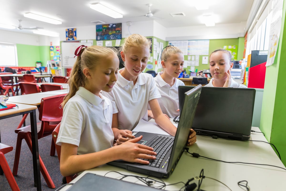 Schoolgirls use laptops in a classroom.