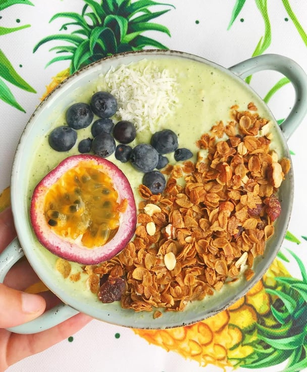 A green smoothie bowl topped with muesli, passionfruit, coconut and blueberries,.