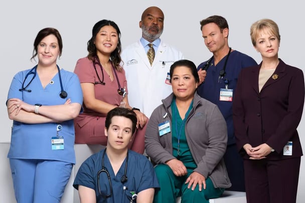 The cast of St. Denis Medical wear medical scrubs and jackets for a promotional photo.