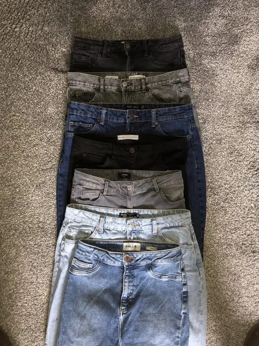 A stack of denim jeans from different brands highlights how clothing waist sizes vary across labels and fit inconsistently.