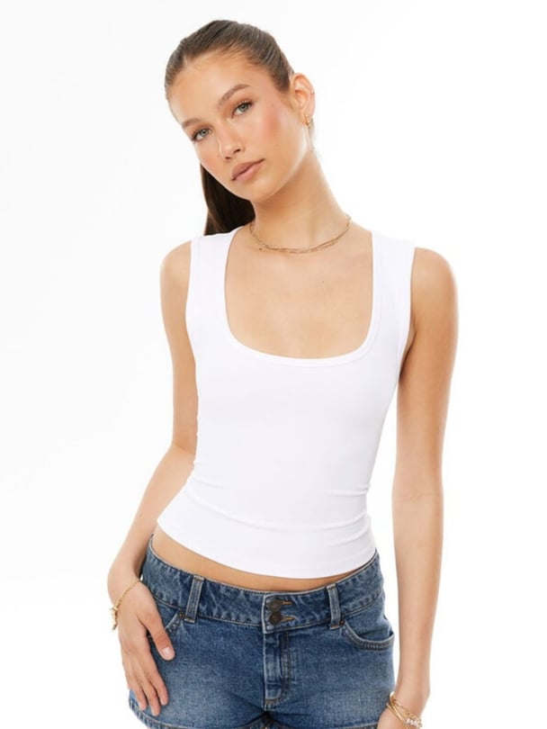 Model wears white scoop neck tank and blue denim shorts.