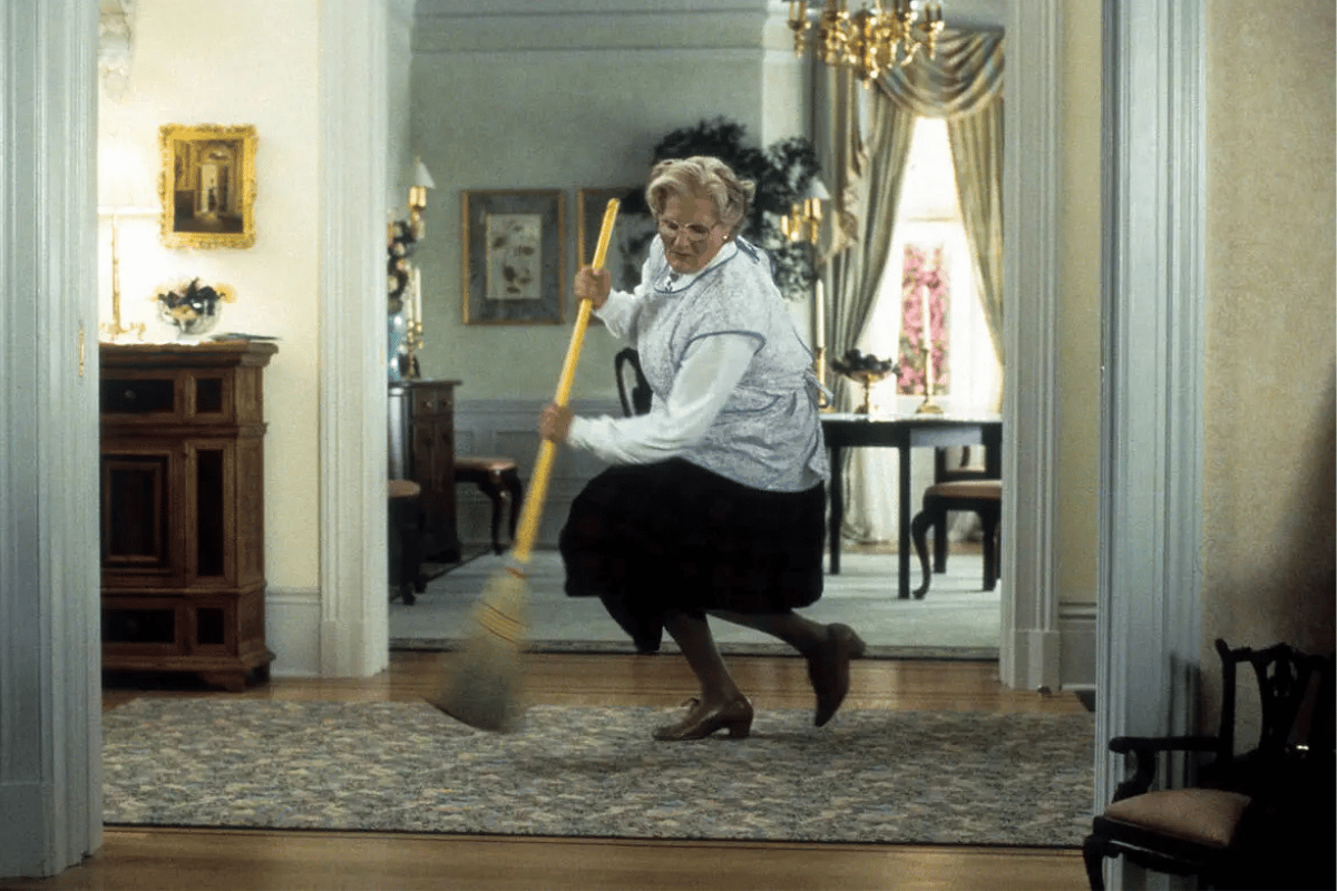 Robin Williams dressed as Mrs Doubtfire, sweeping the hallway.