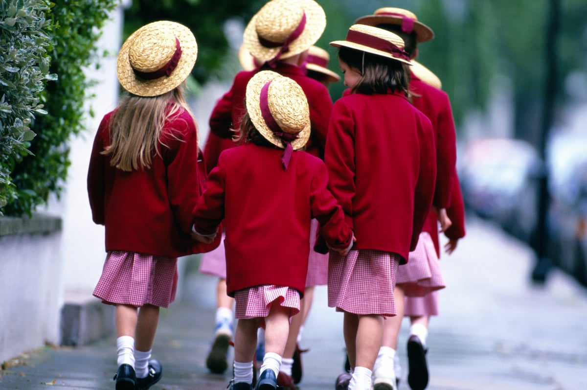 Young private school girls walk down the street in their uniforms.