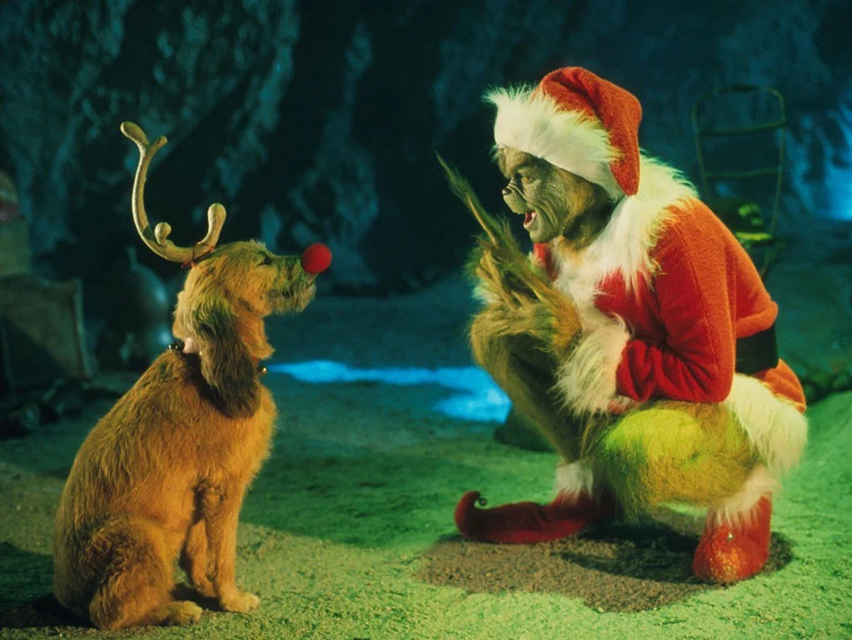 A dog wearing antlers with  The Grinch in a santa outfit. 