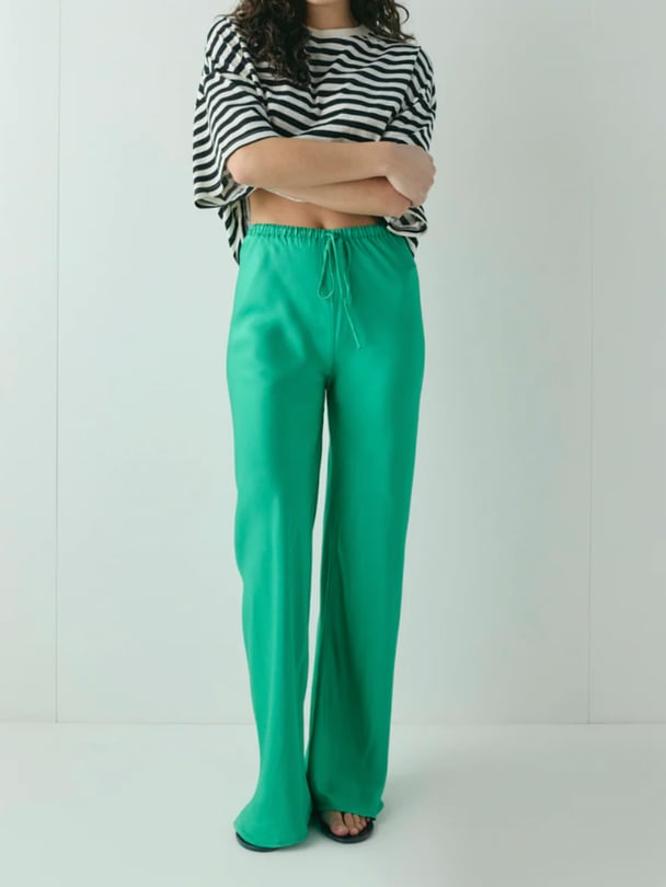 Model wearing bright green satin pants with striped shirt.