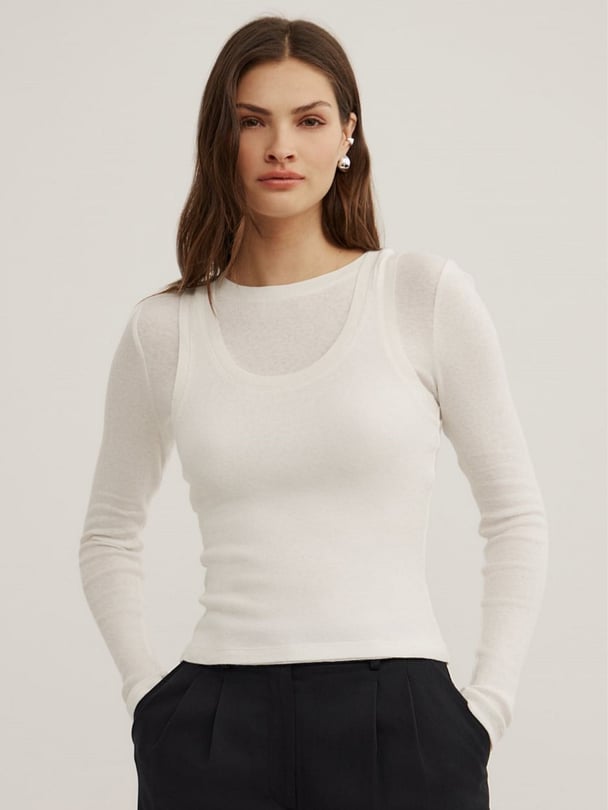 Model wears white long-sleeve top with singlet layer detail.