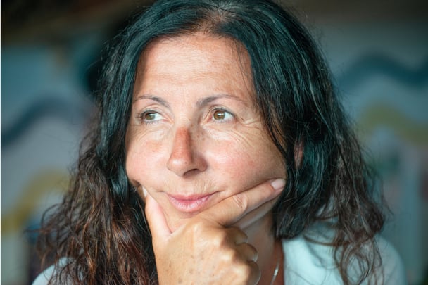Older woman stares off to the side with her face in her hand.