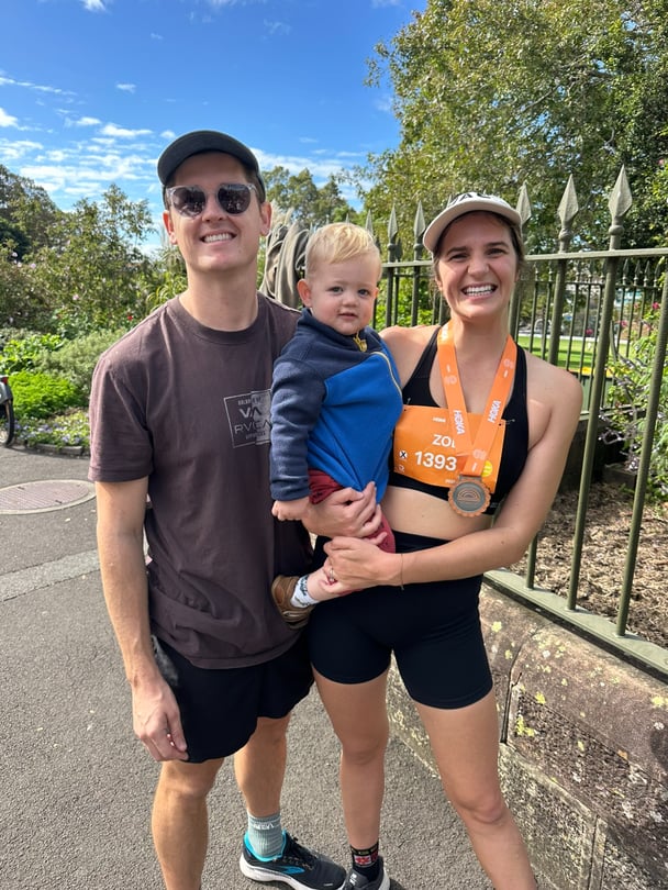 Zoe with her partner and child after her half marathon, wearing a medal.